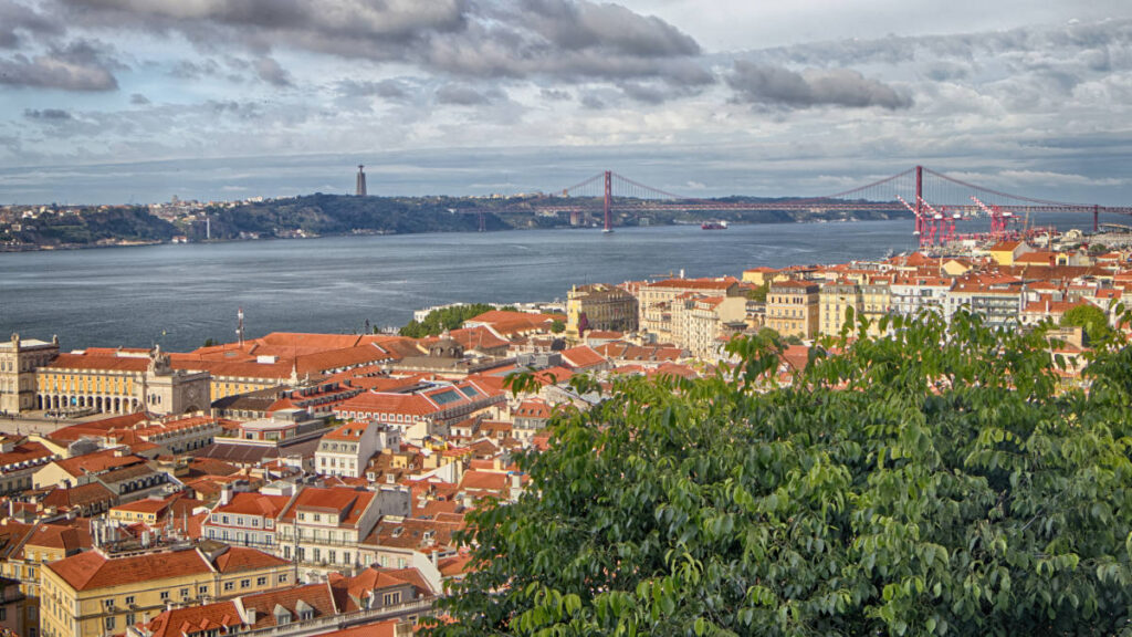 Weitblick vom Castelo über die Baixa bis zur Ponte 25 de Abril und der Cristo-Rei-Statue am gegenüberliegenden Ufer des Tejo.