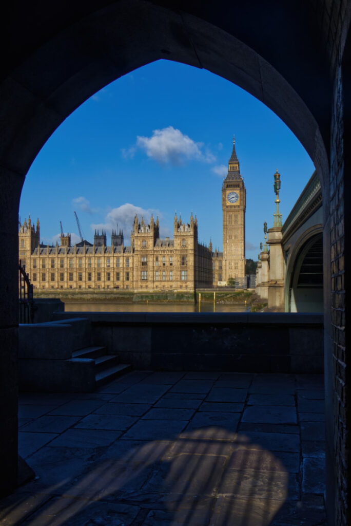 Blick durch den gotischen Westminster Bridge Arch auf Big Ben und den Palace of Westminster, Schattenmuster auf dem Boden, früh morgens, London