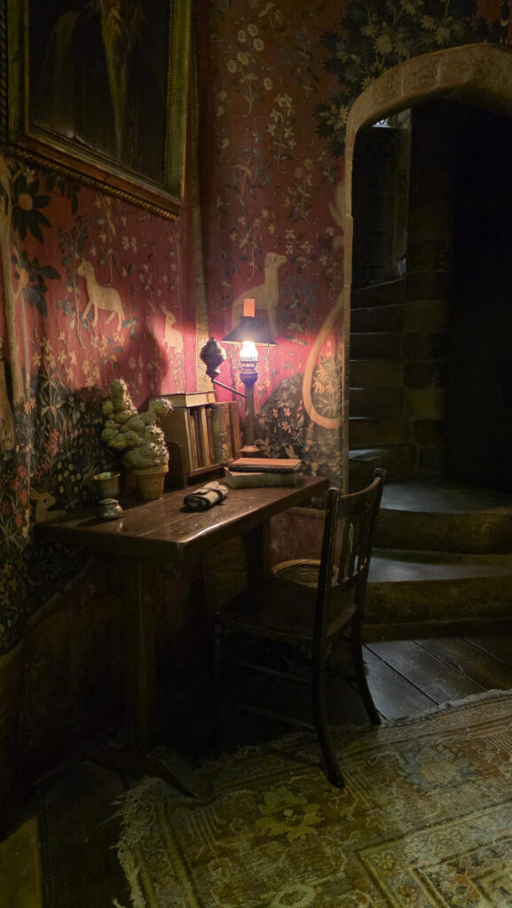 Stimmungsvolle Ecke mit Schreibtisch, Öllampe und Wandteppichen im Gryffindor-Gemeinschaftsraum der Harry Potter Studio Tour London.