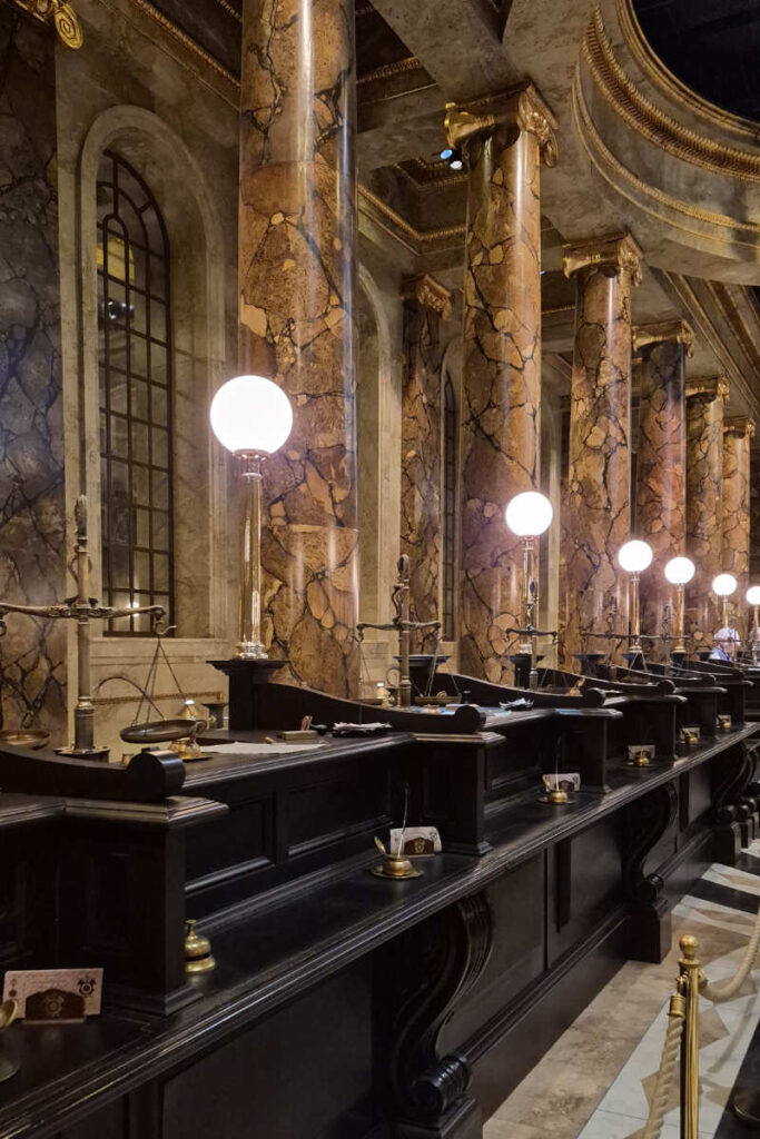 Die schwarzen Kassenschalter mit Marmorsäulen und Kugellampen im Gringotts-Banksaal der Harry Potter Studio Tour London.