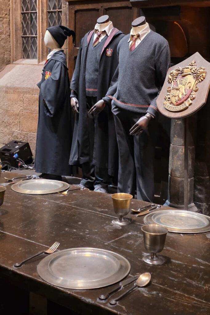 Originale Gryffindor-Kostüme und Hauswappen an den Tischen der Großen Halle in der Harry Potter Studio Tour London.