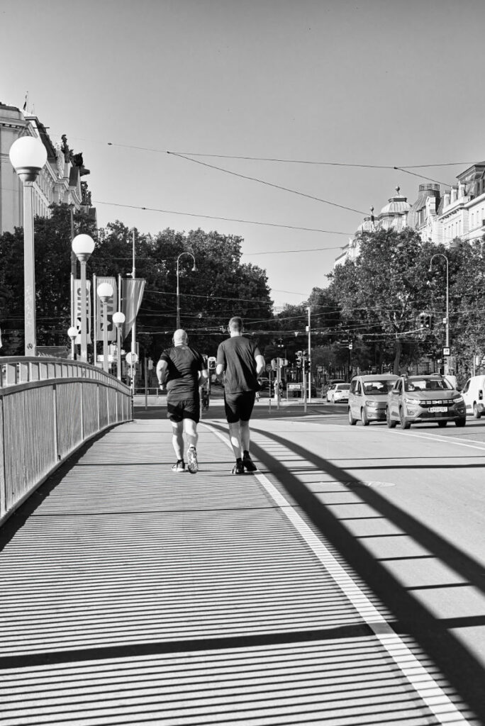 Zwei Läufer von hinten fotografiert auf einer Brücke mit historischen Gebäuden und langen Schatten
