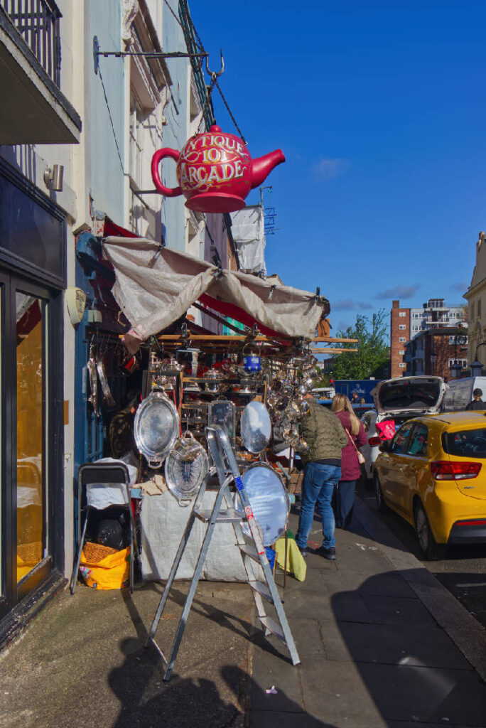 Antiquitätengeschäft in der Portobello Road mit großer pinker Teekanne als Schild und Silberwaren